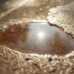 Sunlit puddle on a rough concrete surface slowly drying, visually showing evaporation as water disappears under warm sunlight.