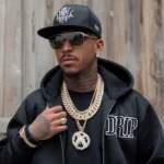 Stylish man wearing sunglasses, a black hoodie with “DRIP” text, and heavy gold chains, representing the slang meaning of “drip” as fashionable style, luxury jewelry, and confident streetwear fashion.